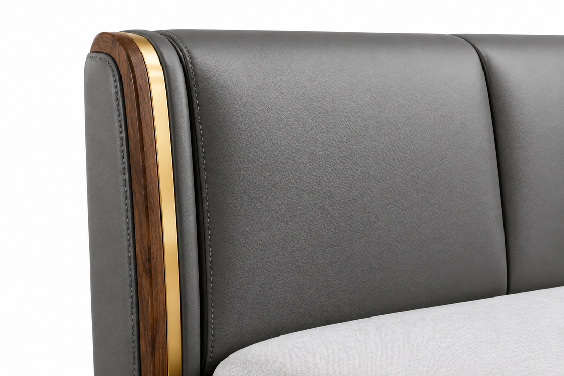 Close-up of gray leather upholstery, stitching, natural wood, and gold accent on the headboard